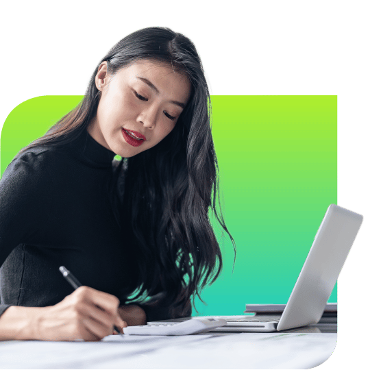 woman taking notes at desk in front of laptop